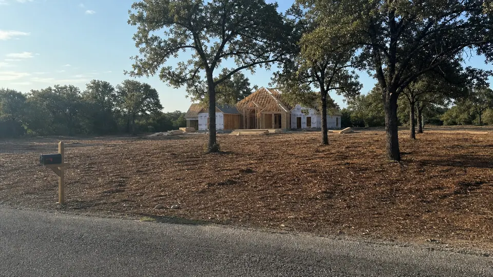 One-acre residential lot cleared of brush with a farmhouse under construction in the background