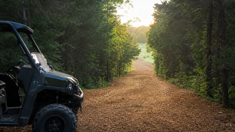 Newly cut ranch road through cedar woods with a mulched surface and a UTV parked at the entrance